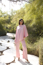 Woman in a pink outfit standing in a garden with greenery and a path.